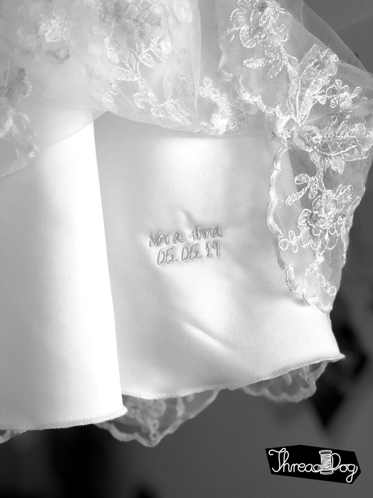 Taufkleid, entstanden aus einem ehemaligen Brautkleid. Im Bildausschnitt ist eine auf dem ersten Unterrock versteckte Stickerei zu sehen. Name des Täuflings und das Datum.